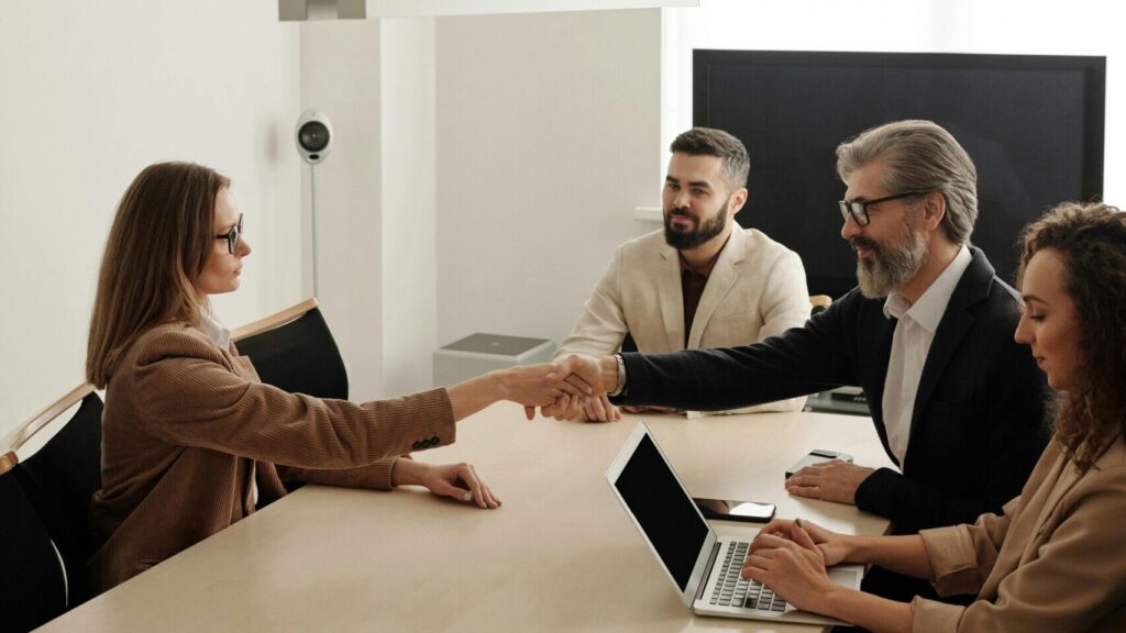 Business professionals engaging in a handshake across a conference table, signifying successful collaboration.