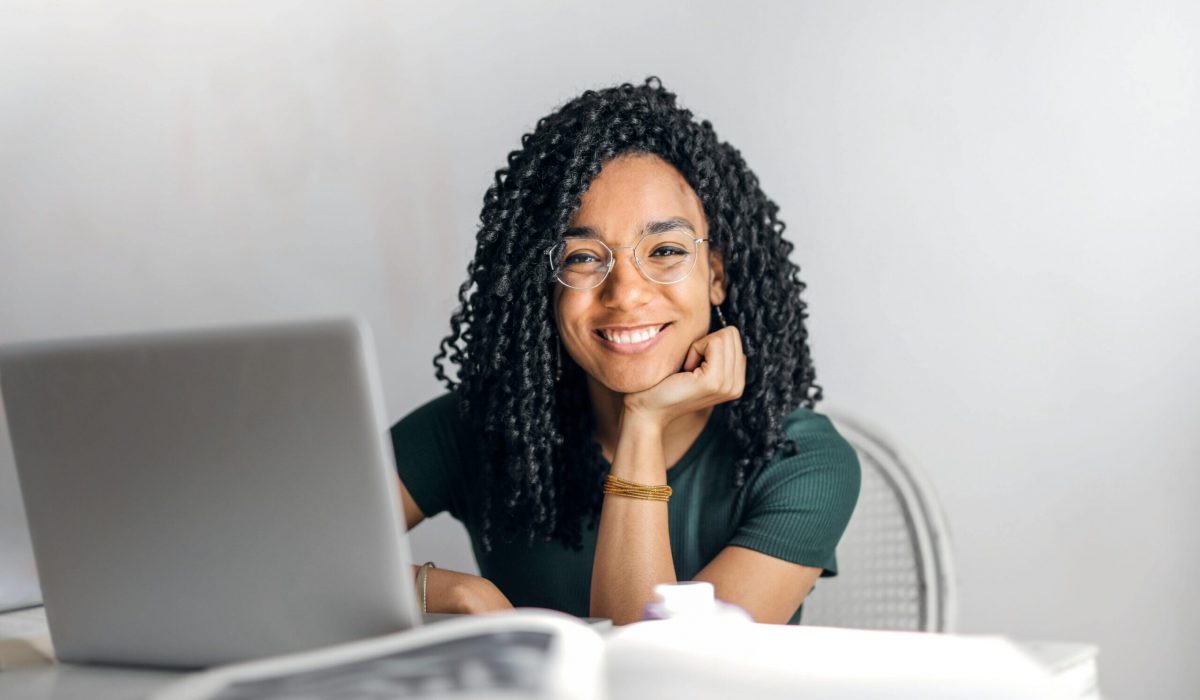 pexels-photo-3769021-3769021 Joyful businesswoman with curly hair smiling at camera while using laptop indoors.